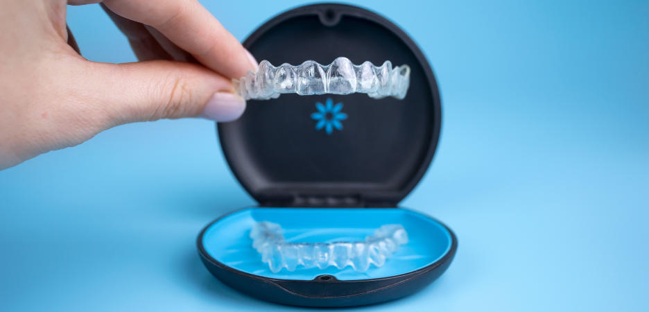 focused image of an Invisalign clear aligner being lifted out of a branded Invisalign box, with a pale blue background