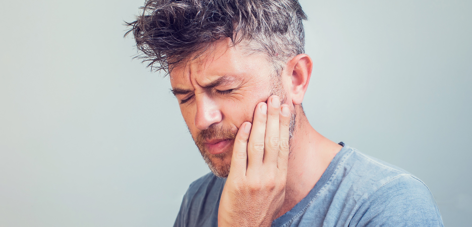 white man wincing with furrowed brow and holding his cheek in pain from tooth ache