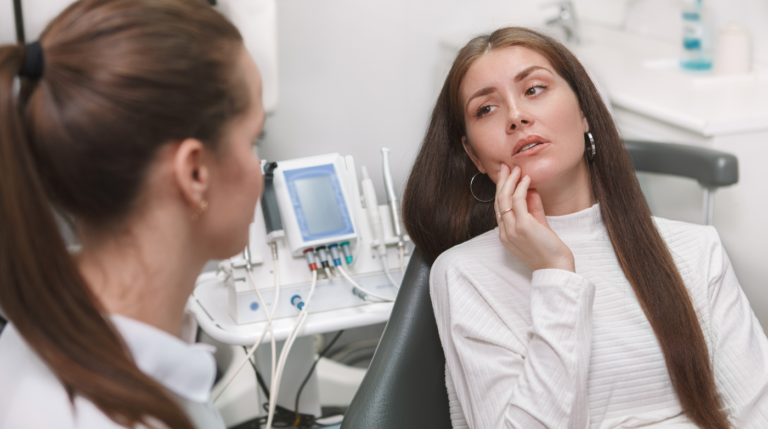 Woman in dental chair holding mouth in pain